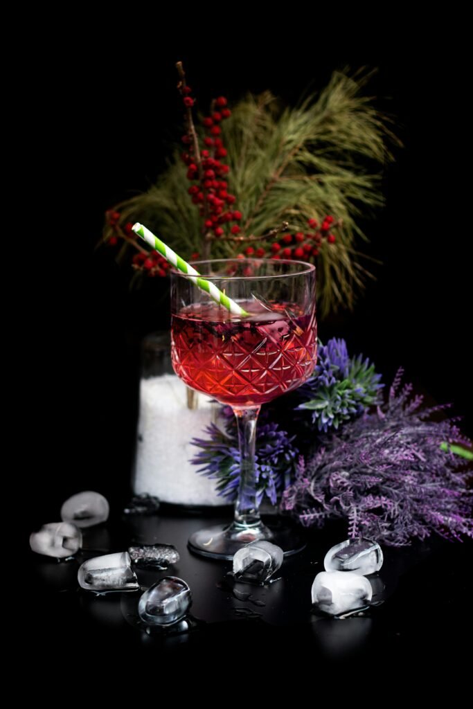 Elegant red cocktail with ice cubes surrounded by winter foliage on a black background.